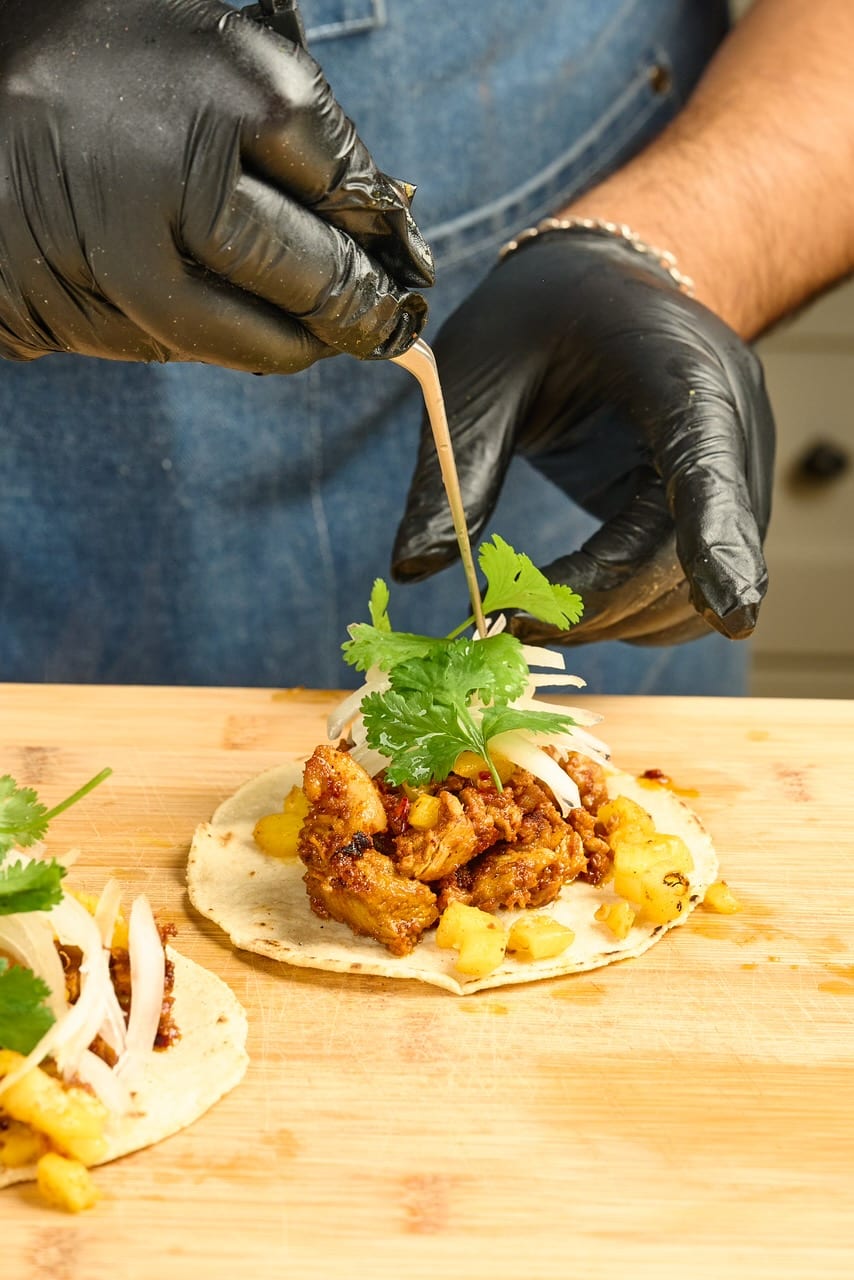 Gloved hands garnishing a taco with cilantro