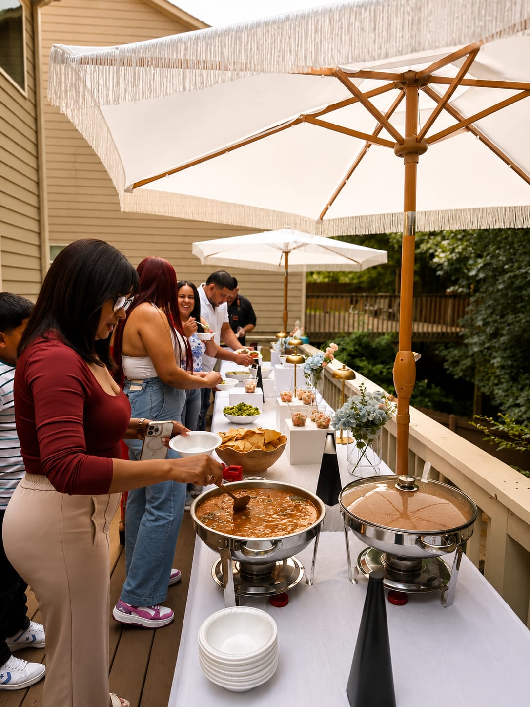 Guests serving themselves at a backyard taco buffet under umbrellas
