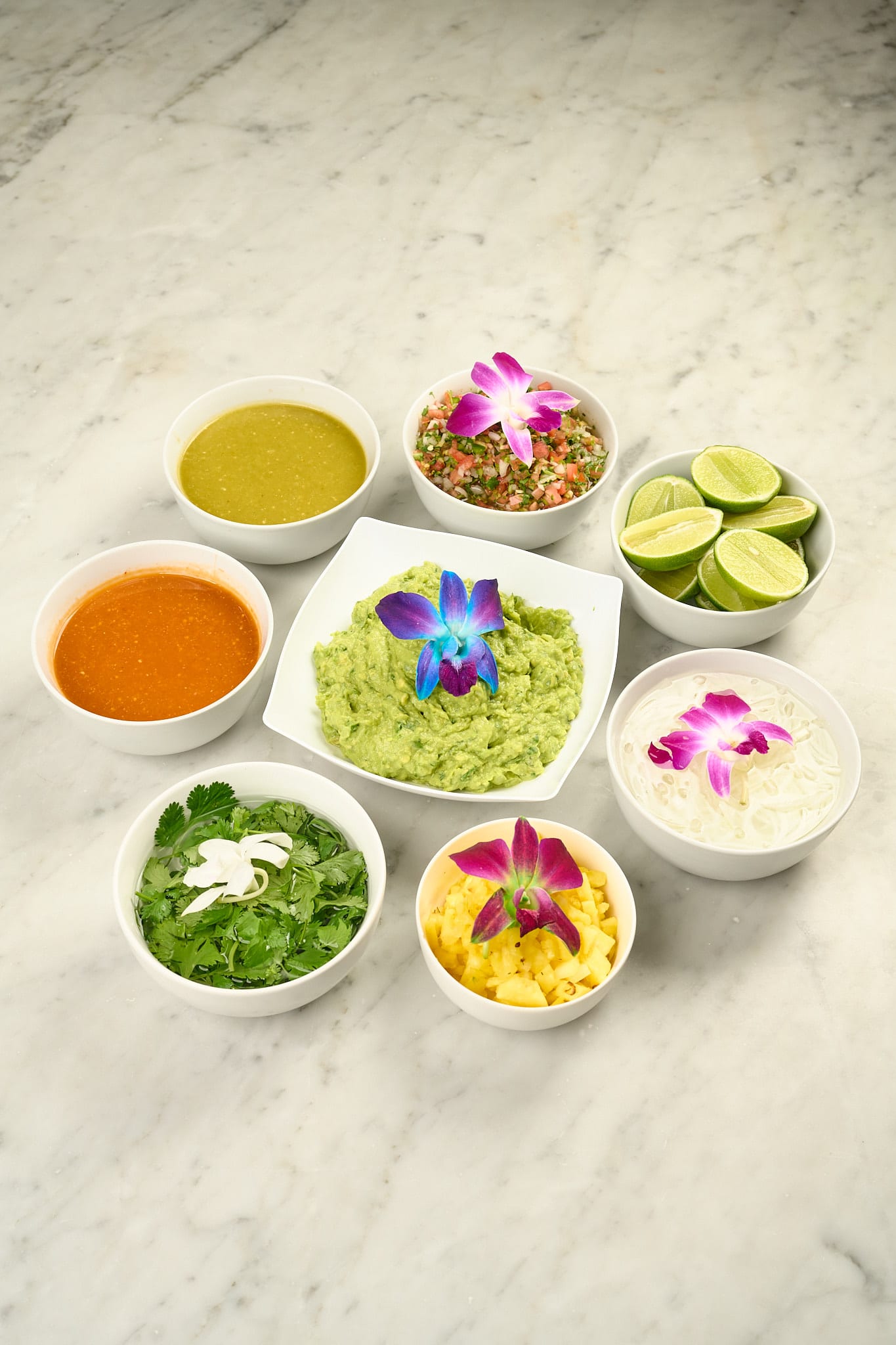 Salsa bar with guacamole, salsas, limes and orchids on marble